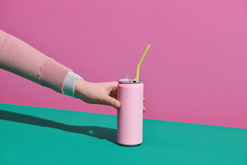 Hand hold soda can with straw on pink background