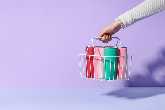 Wire shopping basket full of cans of soft drink in hand