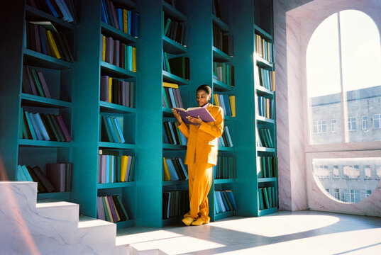 Woman leaning on bookshelf and reading book