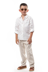 Fototapeta premium Handsome little boy in a muslin shirt, beige pants and leather sandals on a white background. Fashionable modern look!