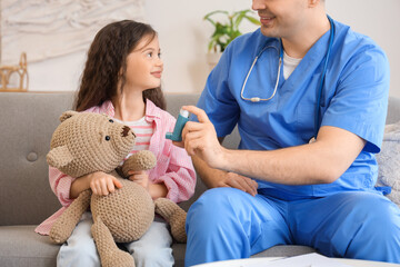 Male doctor giving inhaler to little girl with toy at home