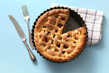 Baking dish with tasty homemade apple pie, napkin and cutlery on blue background