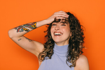 Joyful tattooed woman laughing on orange background