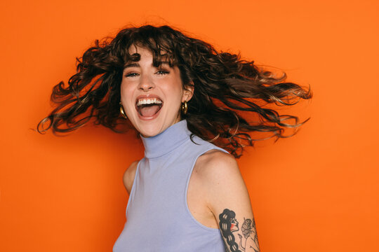 Joyful woman with tattoos laughing against orange background