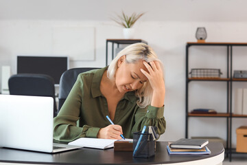 Mature businesswoman experiencing menopause at table in office