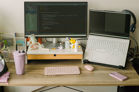 A female programmer's desk with screen, laptop, keyboard, mouse.