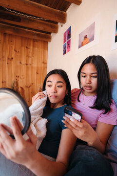 Two young friends at home with phone and cosmetics