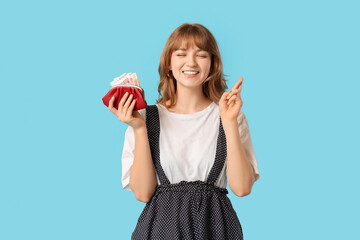 Beautiful young woman holding red purse and raised index finger on blue background