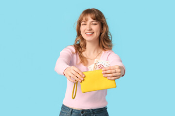 Beautiful young woman holding yellow wallet with money on blue background