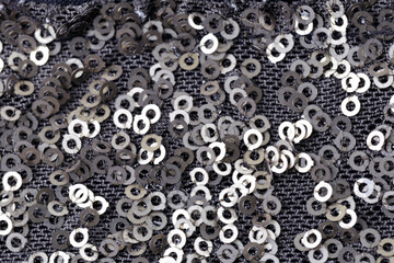 A closeup of a black and silver fabric with many small, bright, round silver beads. The beads are scattered throughout the fabric, creating an intricate, textured design.