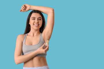 Obraz premium Happy smiling young woman using crystal deodorant on blue background