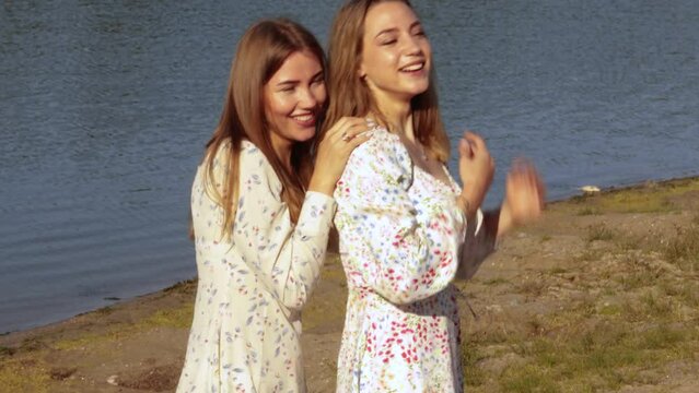 Two pretty women sisters ot friends lesbian couple on beach. Gay girls hugging smiling laughing embracing together girlfriends, dressed flowery dresses, have a date. LGBT concept
