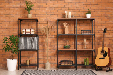 Shelving units, guitar and houseplants near brown brick wall in stylish room