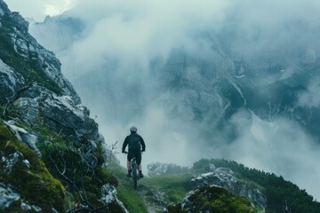 Mountain biker is riding on a mountain ridge trail with his bike, enjoying the view of the clouds in the valley