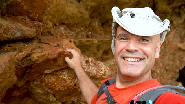 Slow motion, smiling hiker takes a video selfi inside a cave, wearing a sun hat