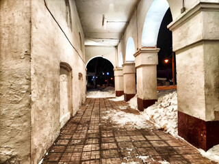 Fototapeta premium Old Ancient Colonnade Pathway at Night. Dimly lit corridor with arches and age-worn columns