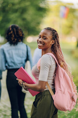 Diverse university student with textbook and backpack at campus looking
