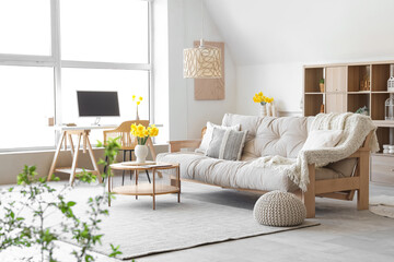 Interior of stylish living room with sofa, coffee table, workplace and vase of narcissus flowers