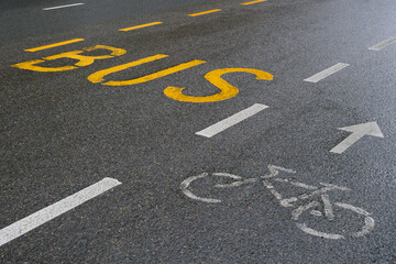 A paved city street with yellow markings designating a bus lane and white markings designating a bike lane.