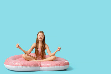Obraz premium Cute little happy girl in swimsuit meditating on inflatable mattress against blue background