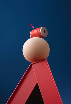 Abstract still life. Red thread reel and beige sphere on triangle
