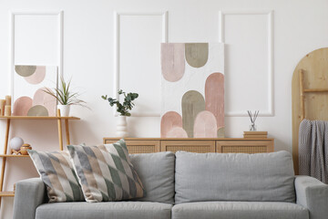 Interior of beautiful living room with comfortable sofa, shelving unit and picture on white wall