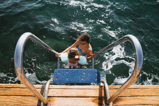 Little girl standing at the bottom of the ladder on a deck by sea