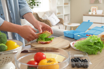 Young man making tasty sandwiches for lunch box in kitchen, closeup