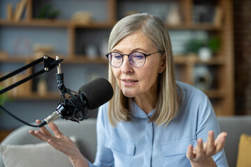 Senior woman records podcast at home, speaking into microphone. She discusses various topics,...