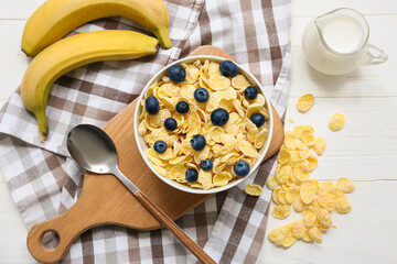 Napkin, wooden board, banana, bowl with cornflakes and berries on white wooden background, closeup