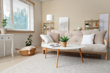 Interior of beautiful living room with comfortable sofa, coffee table, houseplant and pillows