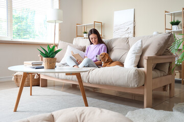 Young woman reading book with cute Beagle dog on sofa in living room