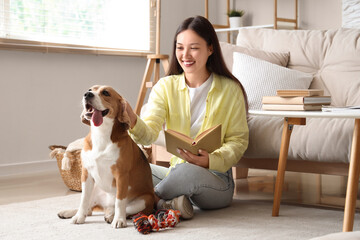 Young woman reading book with cute Beagle dog on floor in living room