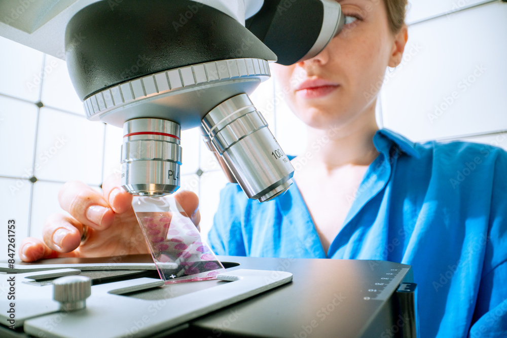 Poster young female laboratory assistant installs a slide glass into a microscope