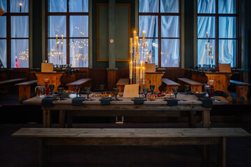 Dobele, Latvia - June 7, 2024 - Elegant dining hall with long wooden tables, floating envelopes and candles, set for a festive meal with glassware and plates. Copy space.