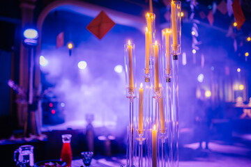 Dobele, Latvia - June 7, 2024 - Close-up of tall candles in glass holders with a purple-lit background, creating a moody and elegant atmosphere at an event. Copy space.