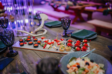 Dobele, Latvia - June 7, 2024 - Close-up of a beautifully arranged appetizer platter with various bites and garnishes on a wooden table set for an elegant event. Copy space.