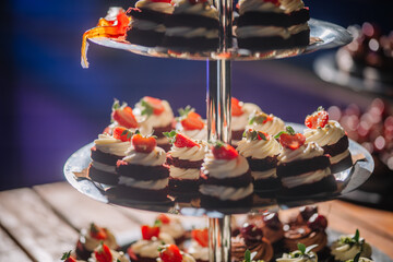 Dobele, Latvia - June 7, 2024 - Close-up of tiered dessert stand with red velvet cupcakes, topped with white frosting and strawberries, under soft lighting. Copy space.