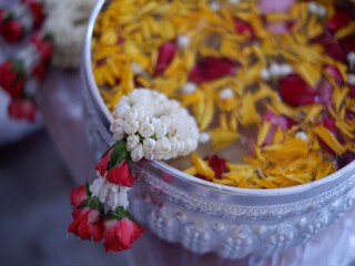Water in a water dipper filled with flowers and flower petals. Songkran Festival in Thailand. Garland of jasmine and roses.