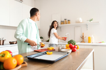 Young Asian woman washing bell pepper and her husband cooking in kitchen