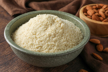 Fresh almond flour in bowl and nuts on wooden table, closeup
