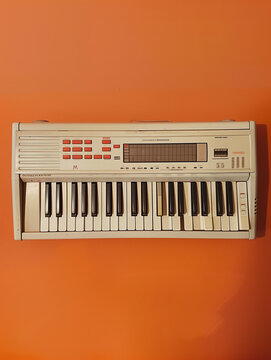 An ivory white vintage electronic keyboard. A throwback worn retro 1980's synthesizer. Isolated on orange background.