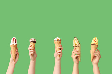 Female hands with different sweet ice-cream in waffle cones on green background