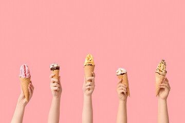 Female hands with different sweet ice-cream in waffle cones on pink background