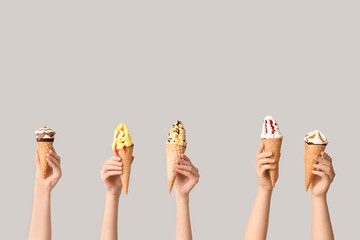 Female hands with different sweet ice-cream in waffle cones on grey background