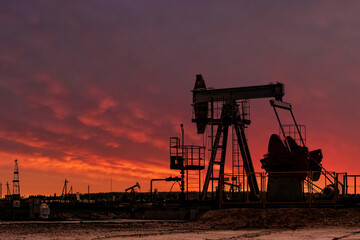 Oil drill rig silhouette and pump jack at sunset background.