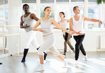 Fototapeta premium Enthusiastic Asian woman enjoying ballet practice with group of amateur dancers in spacious sunlit dance studio ..