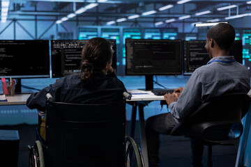 Person with paraplegia and colleague working in inclusive server hub workspace, typing on PC. Woman...