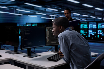 Fototapeta premium IT engineer in server room facility confused by errors on screen while shielding data from potential threats. Perplexed man puzzled by bugs while safeguarding data center hardware against malware