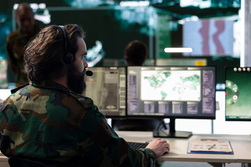 Military staff monitoring real time battlefield operation from CCTV radar system in command center, collecting information for an infantry unit support. Satellite high tech specialist in power base.